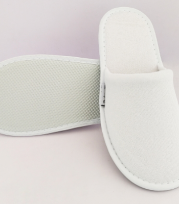 Белые гостиничные тапочки на фоне полотенца